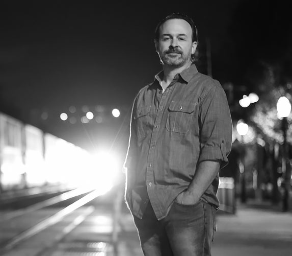 Brian in front of railroad tracks. Train light in the distance.